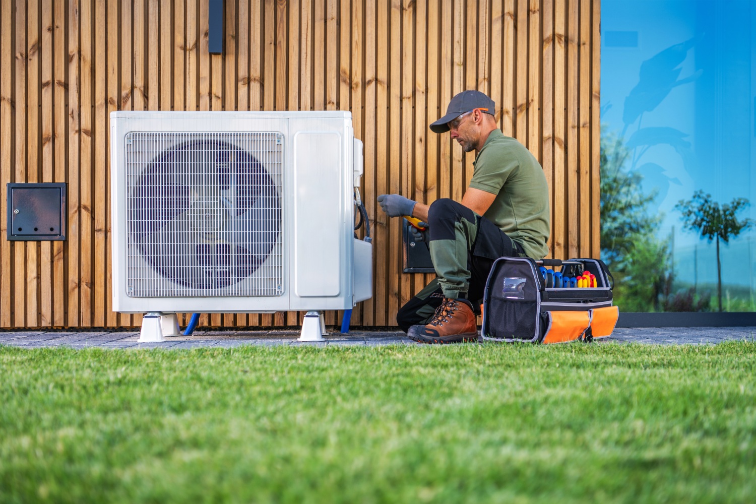 Technician Performing Maintenance on Air Conditioning Unit in Residential Garden During Daytime